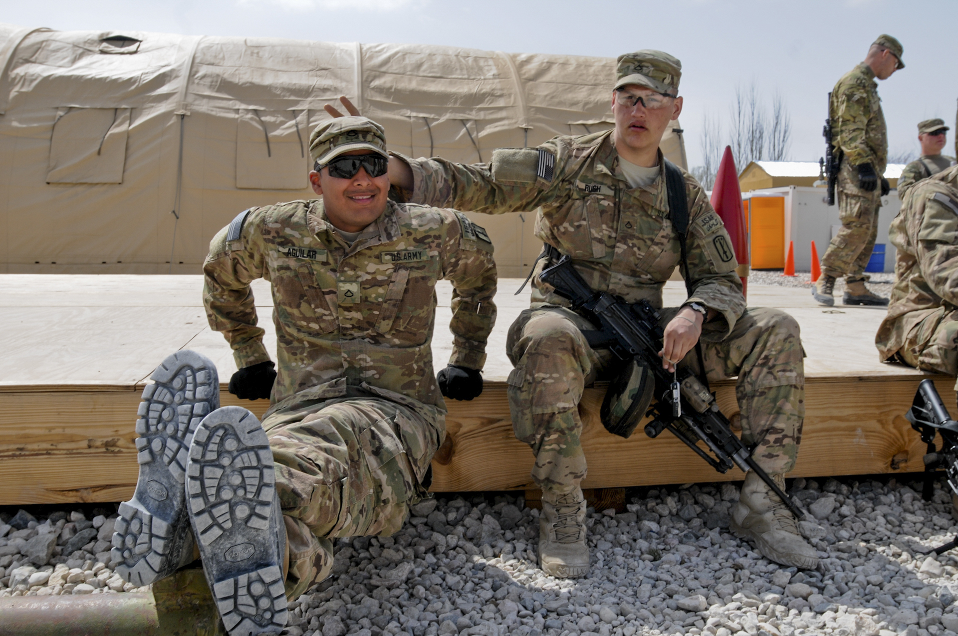 Two men in military fatigues, one holding a firearm, pose for a photo.