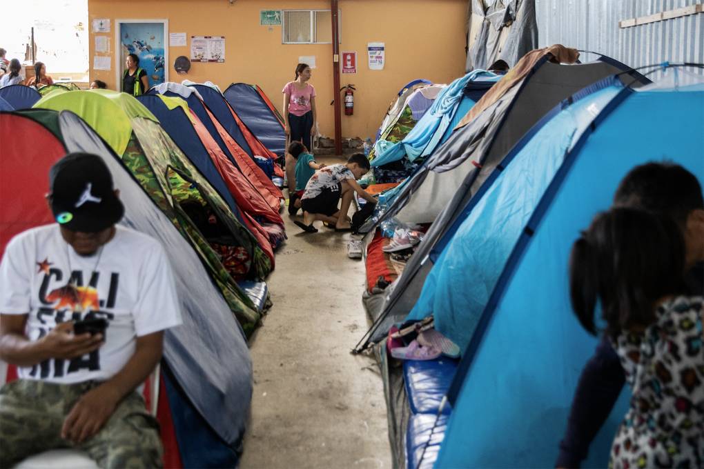 People of various ages are seen in colorful tents in a warehouse.