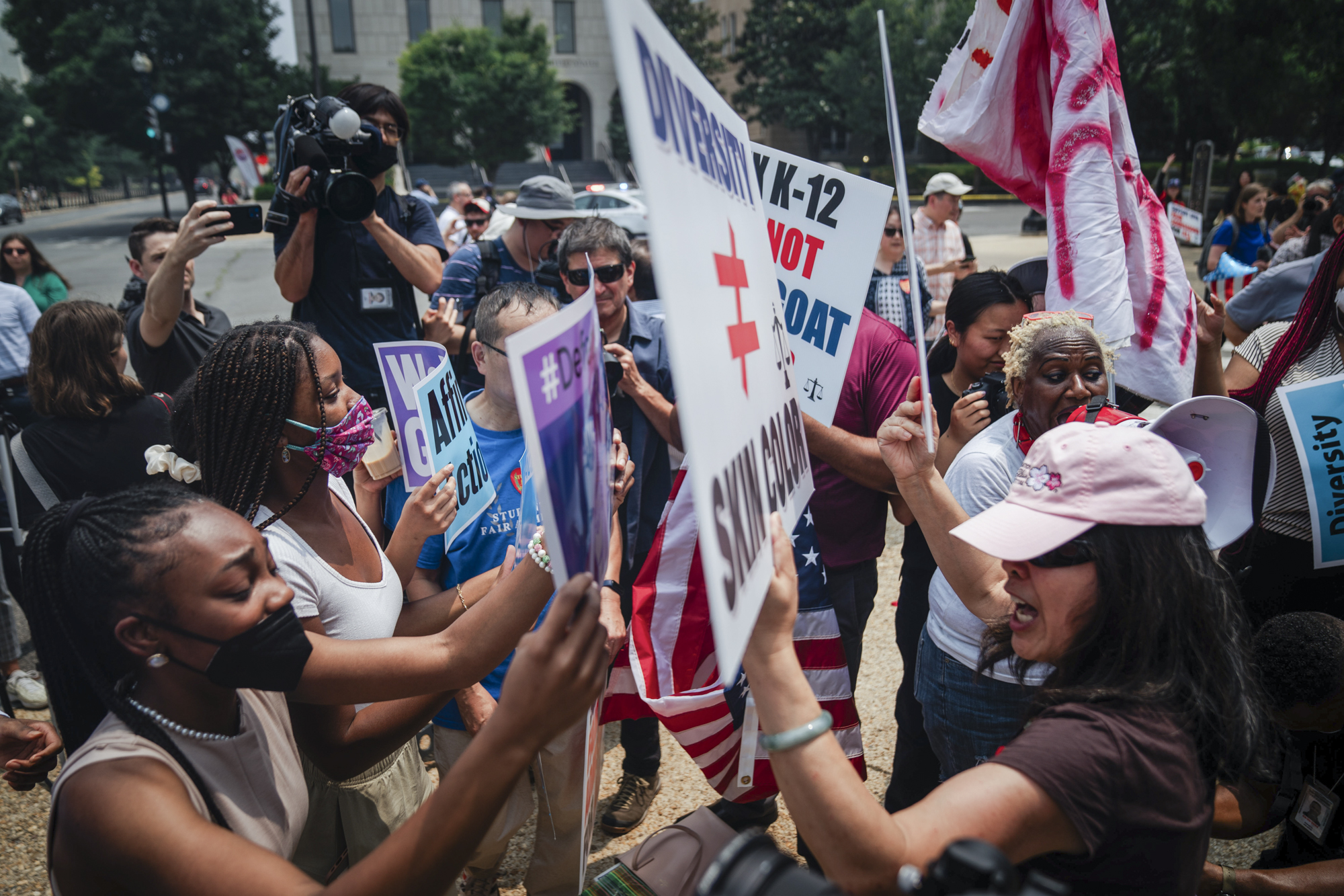 Dozens of people protest holding signs and yelling in each other's faces.