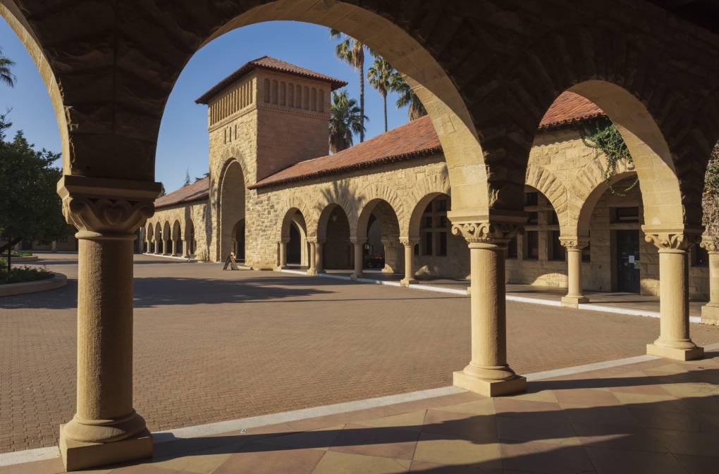 An ornate sandstone colored building with a series of arches sitting on a brick plaza.