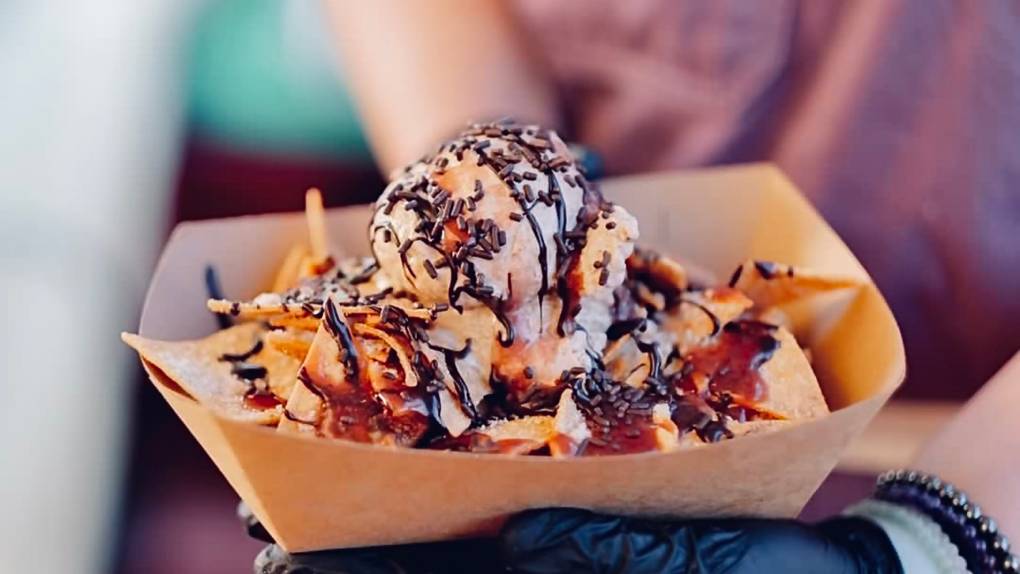 a worker at De La Creamery holds up a plate of ice cream topped with chocolate syrup and cinnamon churro-style tortilla chips