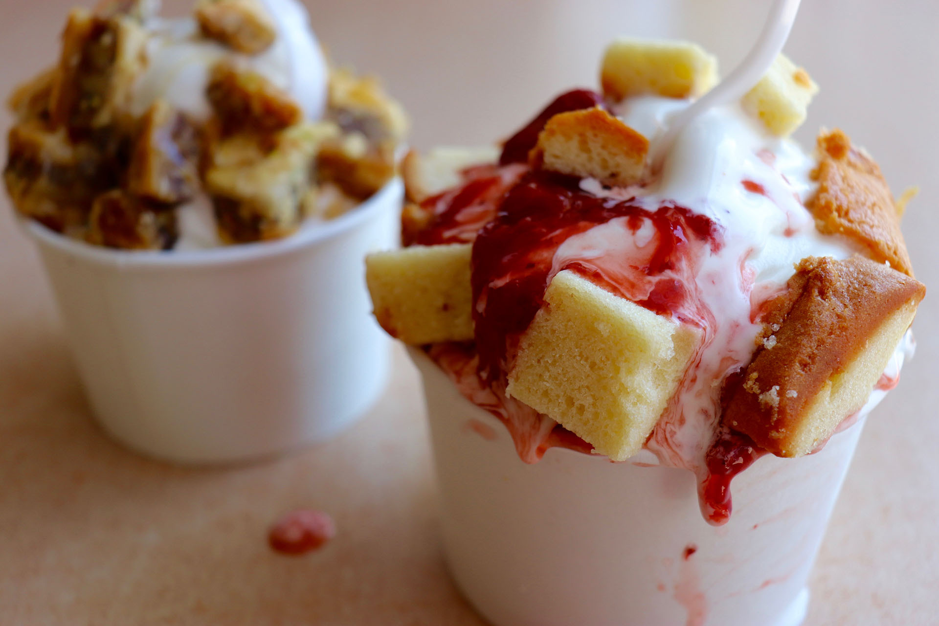 two cups of overflowing soft serve ice cream topped with strawberry cake and baklava 