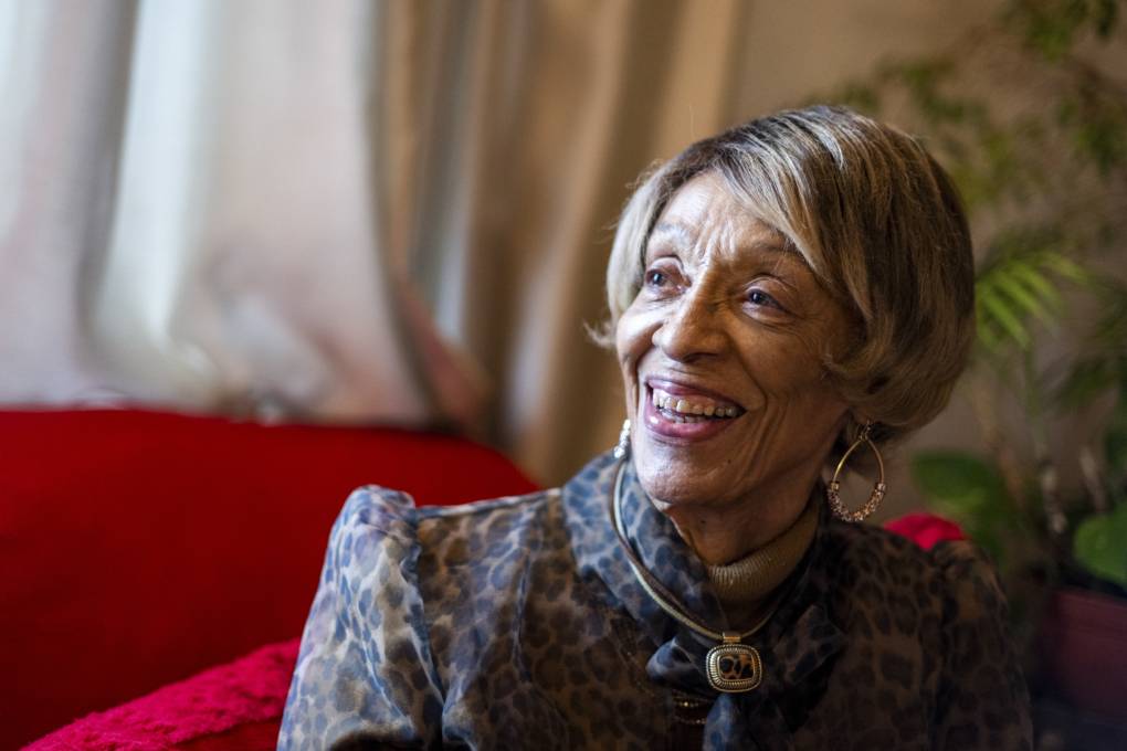 A woman wearing a leopard print top and necklace and earrings smiles while sitting on a red sofa.