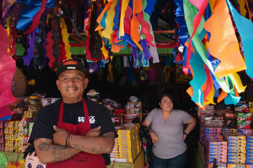 Two people stand in front of a stall full of wares.