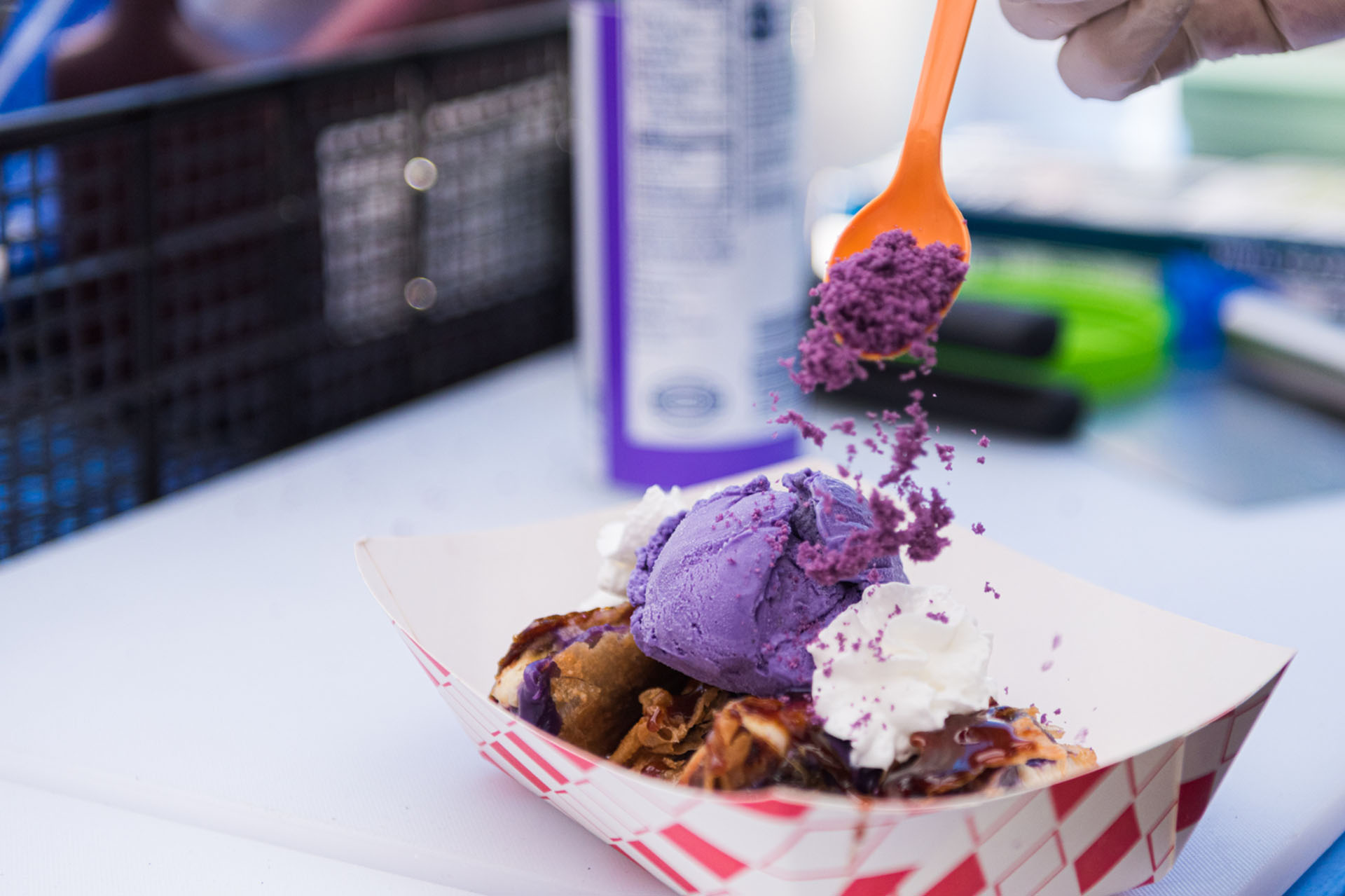 A paper tray of turon (banana lumpia) topped with ube ice cream and sprinkled with ube crumbles.